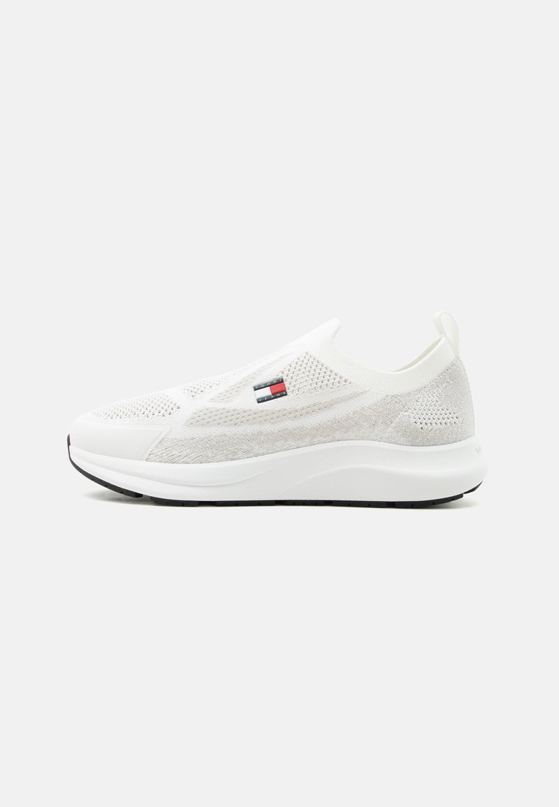 Λευκό χαμηλό αθλητικό παπούτσι τύπου slip-on με πλεκτό πάνω μέρος, ετικέτα με λογότυπο στο πλάι, παχιά σόλα και θηλιά στο πίσω μέρος.