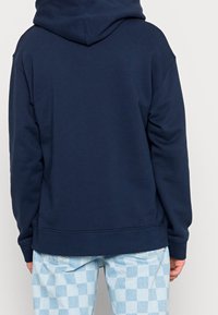 Marinblå sweatshirt i mjukt tyg, med snörning i huvan och ribbade mudd. Bärs med ljusblå rutiga byxor.