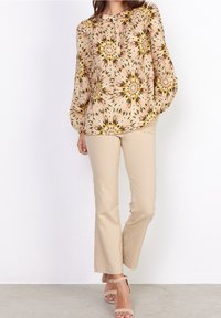 Blusa floreale di un rosa chiaro, con motivi gialli e neri, maniche ample e scollatura rotonda. Abbinata a pantaloni beige a campana.