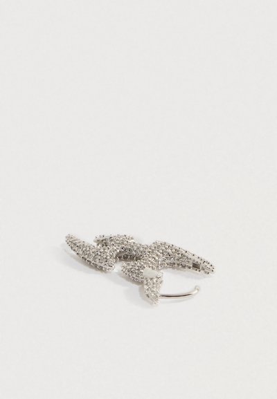 Srebrn lasni sponka v obliki strele, okrašena s prozornimi kamenčki na belem ozadju.