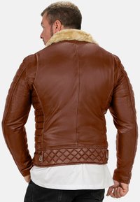 Giubbotto in pelle marrone con colletto in pelliccia sintetica, dettagli trapuntati all'orlo e alle spalle, con una finitura liscia e un design aderente.