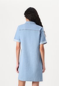 Denimkjole i lyseblå. Korte ermer med rullede mansjetter, kragehals, og lett A-linje silhuett. Glatt tekstur og enkel design.