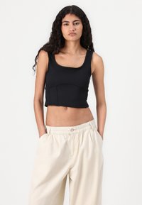 Črn rebrast crop top s kvadratnim izrezom in oprijetim dizajnom, kombiniran s prostornimi bež hlačami z elastičnim pasom.