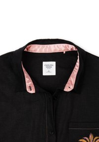 Black shirt featuring a pink satin collar, front pocket with colorful embroidery, and contrasting stitching. Label visible inside collar.