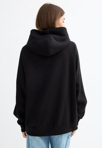 Sudadera negra con capucha de corte holgado, mangas raglán y textura suave. Cuenta con una capucha grande en la parte trasera y dobladillo acanalado.