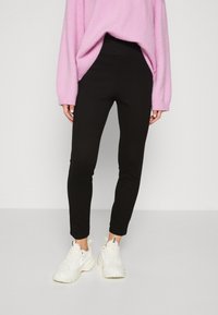 Black leggings made of stretchy fabric, featuring a fitted design. Paired with a loose pink sweater and white sneakers.