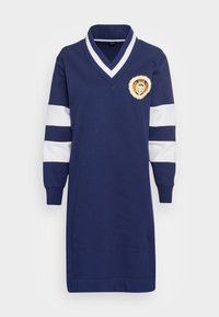 Vestido sudadera azul marino con rayas blancas en las mangas, cuello en V y un emblema bordado redondo con un escudo de león. Material de mezcla de algodón.