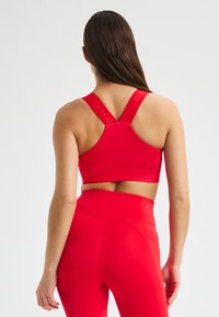 Rode sportbeha met brede banden en een racerback ontwerp. Glad textuur met een strak silhouet. Complementaire hoge taille rode legging.