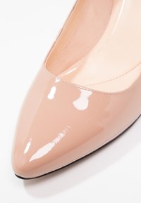 Escarpins en cuir verni beige avec un bout pointu et un décolleté bas, présentant une surface lisse et brillante et une semelle noire.