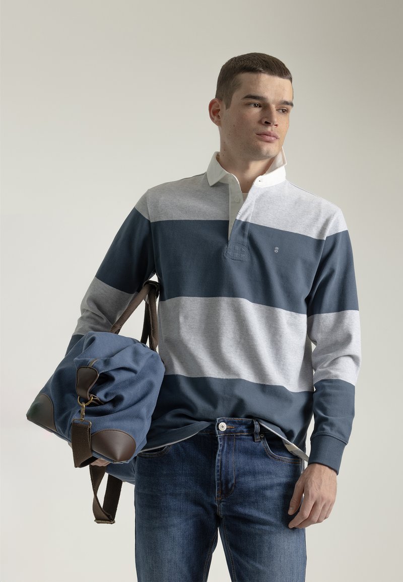 Camisa polo de manga larga con rayas horizontales en gris y azul marino, cuello blanco, combinada con una bolsa azul suave con acentos marrones.