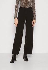 Svarta vida byxor i slät tyg, med en åtsittande midja och en ren, minimal design. Kombineras med svarta klackstövlar.