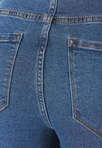 Jeans de mezclilla azul con un diseño ajustado, costuras naranjas en contraste y dos bolsillos traseros con solapas triangulares.