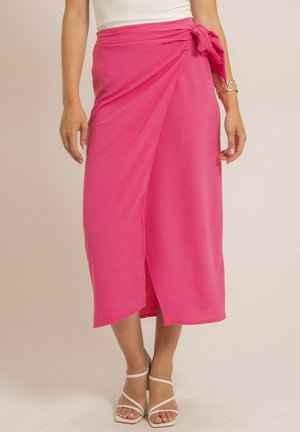 Jupe enveloppante rose en tissu léger, dotée d'un détail de nouage sur le côté, d'un fente pour faciliter les mouvements et d'une silhouette fluide.