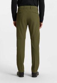 Olivgröna byxor med en slät, matt textur, som har två bakfickor och en rak bendesign, bärs med svarta skor.