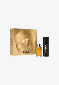 Set regalo Boss The Scent con una scatola dorata e logo in rilievo, che include una bottiglia di profumo color ambra e uno spray deodorante nero.