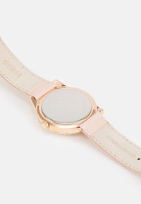 Runde Uhr mit einem rosevergoldeten Gehäuse, glattem silbernem Rückdeckel und einem hellrosa Echtlederarmband mit geprägtem Text.