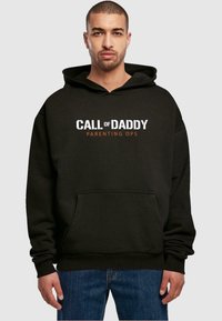 Czarna bluza z kapturem z przednią kieszenią, z napisem "CALL of DADDY" w białym kolorze i "PARENTING OPS" w pomarańczowym. Miękki materiał, luźny krój.