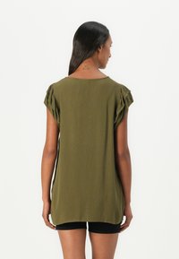 Olive rohelise lühikeste varrukatega särk, tekstuuriga kangast, laia lõikega ja volangidega varrukates. Hemline on kaardus, ulatudes puusadest allapoole.