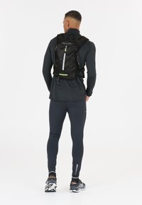 Black backpack with a mesh design, featuring a front pocket, reflective accents, and adjustable straps. Worn by a person in athletic attire.