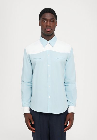 Cămașă bleu deschis, cu yoke și manșete albe, având guler, două buzunare frontale și o textură netedă.