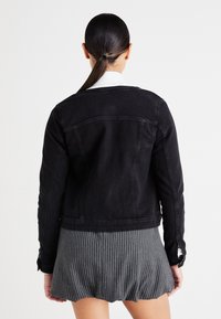 Μαύρο τζάκετ από τζιν με στενή γραμμή και κουμπωτά μανίκια, με ραμμένα ράμφη και κλασικό γιακά. Φοριέται πάνω από μια φούστα με ρίγες.