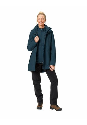 Dark blue waterproof jacket with a hood, front zipper, and side pockets. Paired with black pants and brown hiking boots.