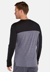 Langärmliges Hemd mit einem schwarzen oberen Bereich und einem grauen strukturierten unteren Teil. Hergestellt aus weichem Stoff mit seitlichen Schlitzen für Bewegungsfreiheit.