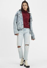 Lichtblauwe denimjack over een bordeauxrode coltrui, gecombineerd met versleten lichtblauwe jeans en beige platformlaarzen.