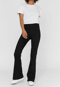 Svarta utsvängda jeans med hög midja, parat med en vit t-shirt med rund hals och vita sneakers. Slät tygtextur, avslappnad design.