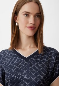 Granatowa bluzka V-neck z krótkimi rękawami, z teksturowanym wzorem w białym kolorze. Z kontrastowym wykończeniem dekoltu. Gładkie wykończenie materiału.