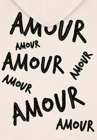 Krém színű kapucnis pulóver, amelyen a "AMOUR" szó fekete hímzése ismétlődik különböző méretekben és irányokban az anyagon.