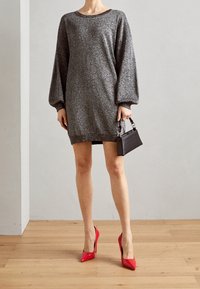 Třpytivé šedé oversized šaty s balónovými rukávy, doplněné černou kabelkou a lesklými červenými lodičkami. Texturovaná látka, volný střih.