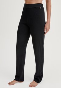 Zwarte, gebreide loungebroek met een hoge elastische tailleband en een kleine metalen accent. De stof lijkt zacht en iets structuur te hebben.