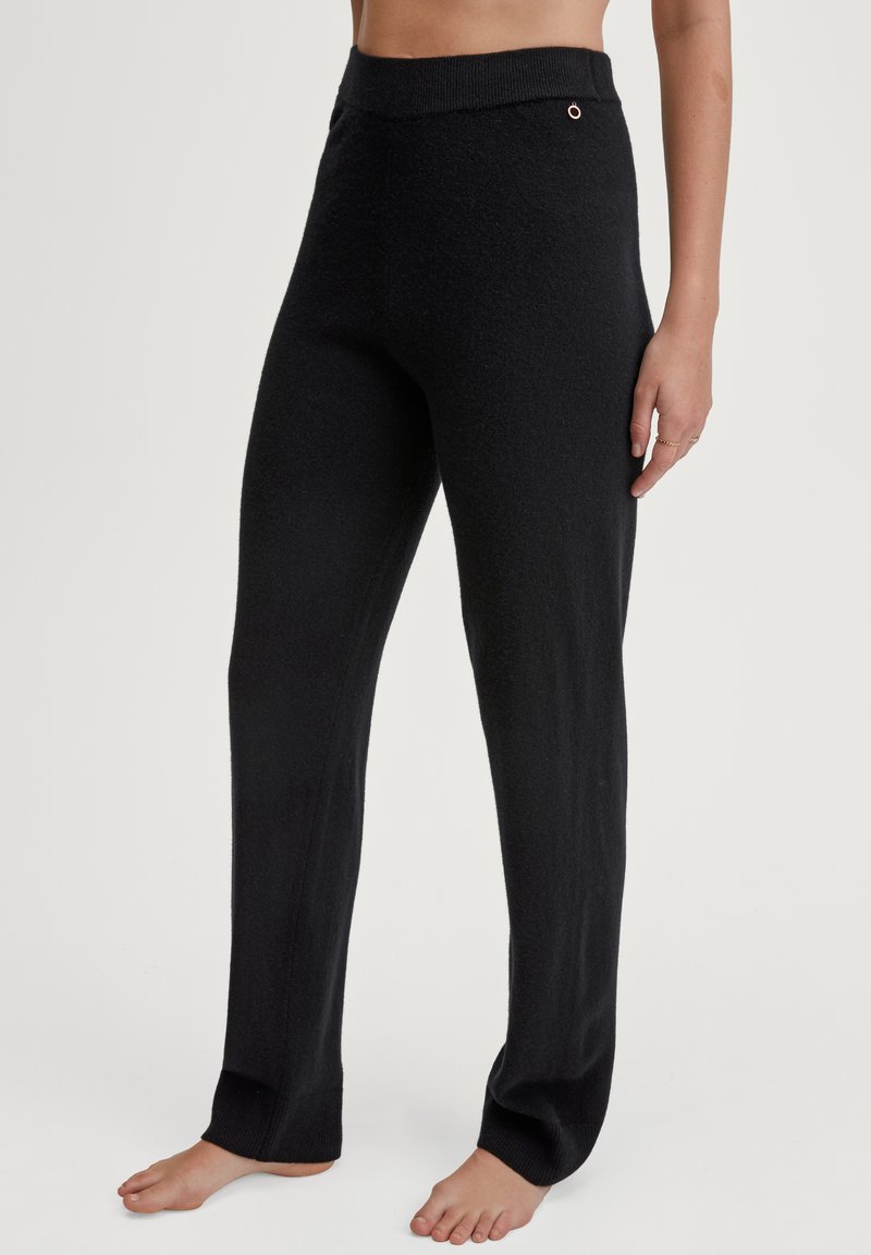 Zwarte, gebreide loungebroek met een hoge elastische tailleband en een kleine metalen accent. De stof lijkt zacht en iets structuur te hebben.