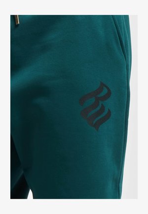 Teallin joggerit, valmistettu pehmeästä kankaasta, sen vasemmassa alalaidassa on musta kuviollinen logo.