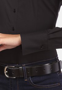 Zwarte lange mouwen shirt met knopen, met geplooide manchetten. Gecombineerd met een zwarte leren riem en donkerblauwe denim jeans met oranje gestikte naden.