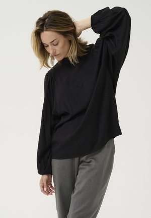 Zwarte blouse met lange mouwen en hoge hals, met een gestructureerd ruitpatroon en een ontspannen pasvorm, gecombineerd met lichtgrijze broek.