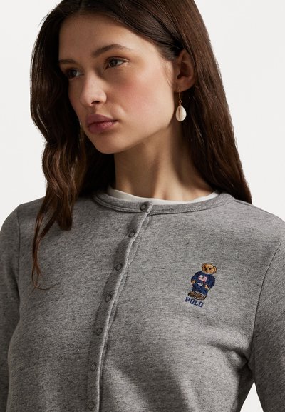 Cardigan grigio con bottoni realizzato in tessuto morbido, caratterizzato da un piccolo orsetto ricamato con una giacca blu e la scritta "Polo".