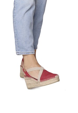 Red fabric wedge sandals with a jute platform, featuring crisscross beige straps and stitched detailing. Seen on a foot with light denim.
