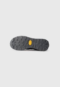 Semelle de chaussure noire robuste avec des profils profonds et un logo Vibram jaune central, présentée sur un fond blanc uni.