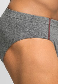 Slip in cotone grigio con una texture liscia, design a vita bassa e cuciture rosse a contrasto lungo l'elastico. Taglio e silhouette minimalisti.