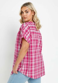 Camicia a maniche corte a quadri rosa con una vestibilità rilassata, caratterizzata da un colletto, fessure laterali e un dettaglio con spacco sulla schiena. Realizzata in tessuto leggero.
