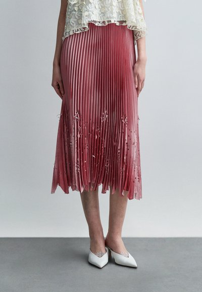 Jupe plissée dégradée rose avec une broderie florale délicate à l'ourlet. Associée à des talons blancs à bout pointu, ornés de détails en dentelle.