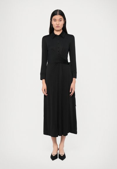 Rochie neagră, cu mâneci lungi și cu înfășurare, prevăzută cu nasturi în față și cordon din material în talie. Textură netedă și design până la gleznă. Pantofi negri ascuțiți.