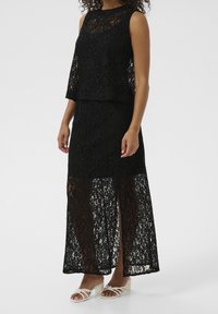 Abito a due pezzi in pizzo nero con top senza maniche e collo alto, accompagnato da una gonna lunga con un motivo floreale trasparente. Orlo rifinito.