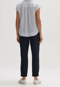 Vaaleanharmaa kauluspaita lyhyillä hihoilla, takakaarroke, yhdistettynä tummansinisiin kapeneviin housuihin ja valkoisiin tenniskenkiin. Pehmeä rakenne, rento muotoilu.