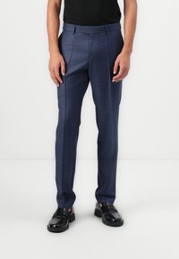 Pantalones de cuadros azul marino hechos de una tela suave, con frente plano, corte ajustado y bolsillos laterales, combinados con zapatos de cuero negro.