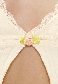 Κοντινή λήψη ύφανσης κρεμ με δαντέλα, με ένα μικρό ροζ κορδέλα τριαντάφυλλο και πράσινα φύλλα στη μεσαία άνοιξη.