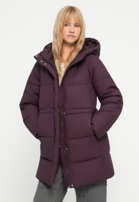 Lilla puffjakke med hette, med glidelås foran, trykknapper og sidelommer. Teksturert, quiltet design for isolasjon.