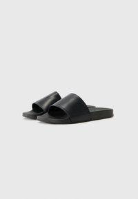 Svarta slidesandaler med ett omlott läderövre, öppen tådesign, texturerad svart gummisul och minimalistisk konstruktion.